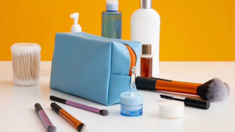 Cosmetic products, skincare containers, and makeup brushes arranged alongside a cosmetic toiletry bag.