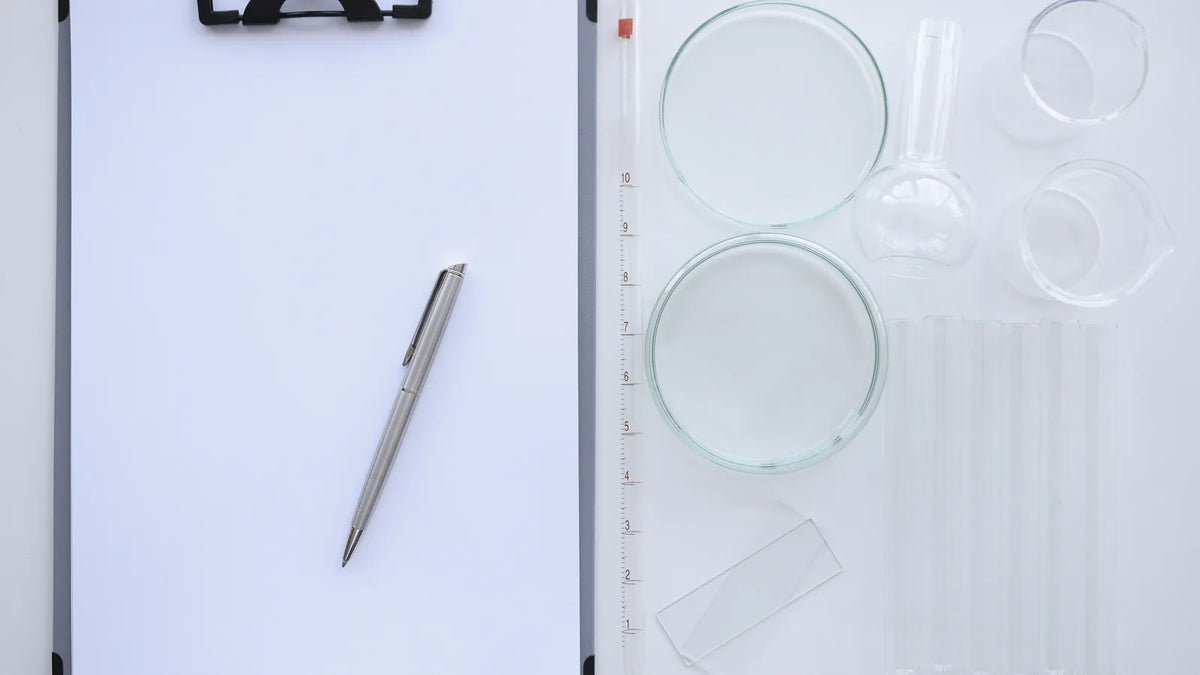 Clipboard with a blank sheet and pen beside laboratory glassware, illustrating when cosmetics need a safety data sheet (SDS)