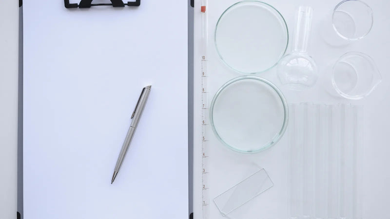 Clipboard with a blank sheet and pen beside laboratory glassware, illustrating when cosmetics need a safety data sheet (SDS)